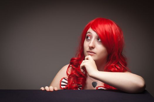 Portrait of an Attractive Red Haired Woman Looking Up with Her Hand on Chin on a Grey Background.