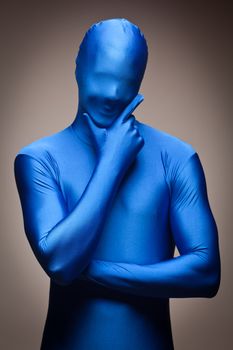 Thinking Man with Hand on Chin Wearing Full Blue Nylon Bodysuit on a Grey Background.
