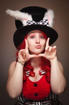 Attractive Red Haired Woman Wearing Bunny Ear Hat and Framing Her Face with her Hands on a Grey Background.