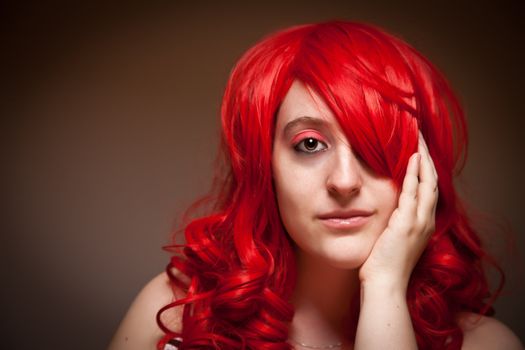 Portrait  of an Attractive Red Haired Woman with Her Hand on Her Face on a Grey Background.