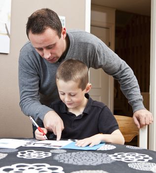 Father helping son with his homework sitting in at the table