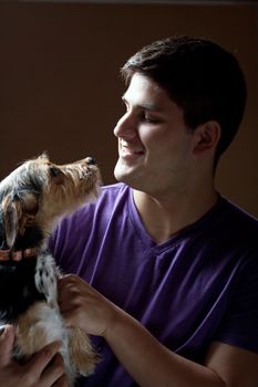 Low key portrait of a young man holding a cute mixed breed terrier dog isolated over a dark background.