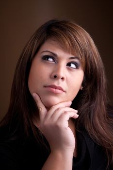 A pretty young Hispanic female posing with her hand on her chin thinks deeply about something on her mind.