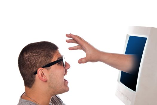 Nerdy young man looks frightened as a hand and arm reaches out from his computer monitor.  A great concept for identity theft or spyware.