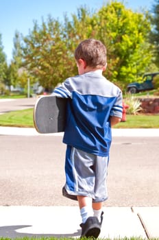 Cute little boy walking out to the street to ride his skateboard just like his hero, his teenage brother.