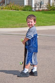 Cute little boy with his skatboard on a suburban street.