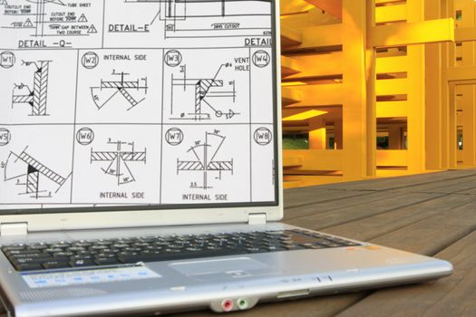 Welding works on computer with steel fabrication as background.