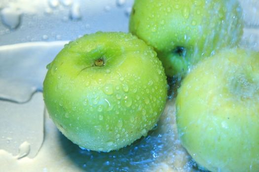 Water splashing onto a green apple in blue tint background.