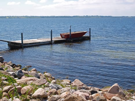 Small wooden jetty dock with a dingy boat sea ocean background