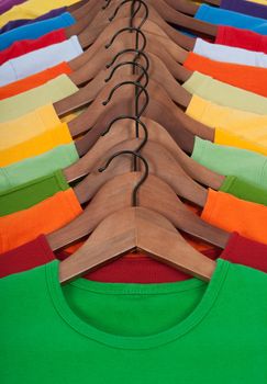 Choice of vibrant colorful t-shirts on wooden hangers.