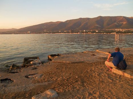 tourist sitting on a sea beach and looking on sea, mountains and town