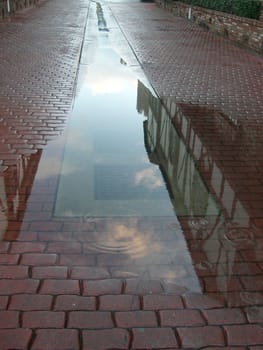 A rain puddle in the middle of a cobblestone street.