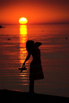 Girl with slippers in her hand is posing on the sea