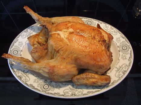 Freshly roasted chicken on plate against black background