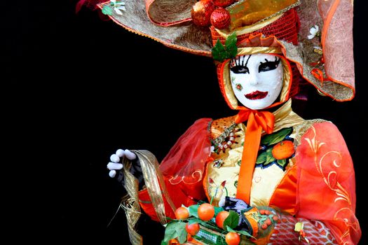 A masked woman dressed in orange, with a basket at the Venice Carnival