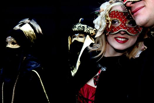 A masked couple, the lady with a red mask, black background, at the Venice Carnival