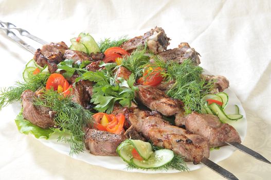 Hot dish of pieces of lamb on skewers in a dish served with vegetables.