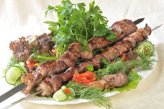 Hot dish of pieces of lamb on skewers in a dish served with vegetables.