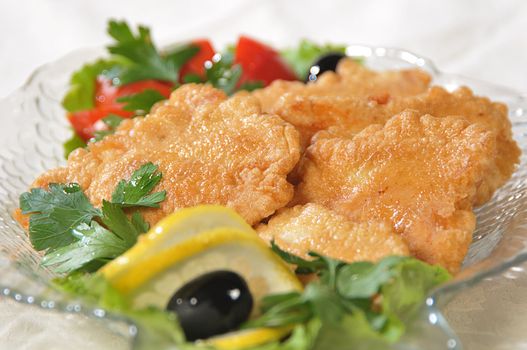 Pieces of fish filet are fried in an egg and decorated a tomato, greenery and olives