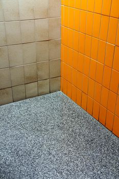 Corner of a public bathroom where three different coverings meet, orange and beige tiles with a speckled vynil floor. Funky!