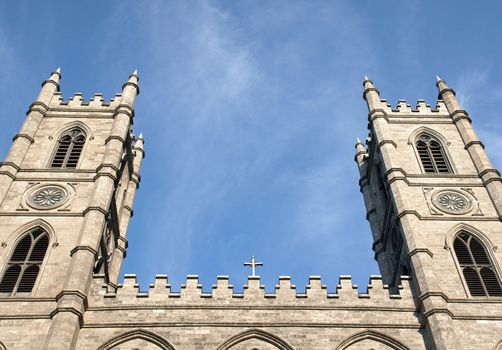 Looking up at old stone Christian church symetrical bell towers contrasted by bright blue sky