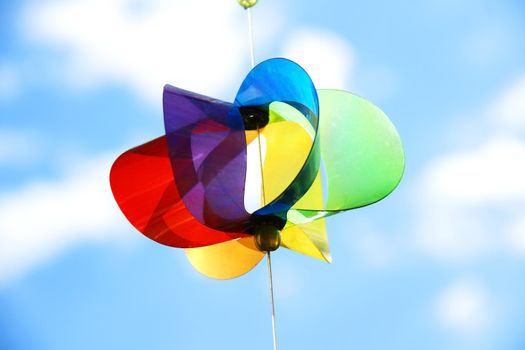 Translucent rainbow colored plastic pinwheel shot against the sky. A wind Kid toy in the backyard.