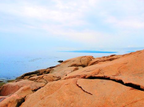 Beautiful orange color rock formation right by the calm sea on a foggy morning.