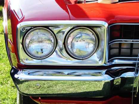 Close-up on the headlights and the chrome bumper of a Hot rod bright red car at a meet show