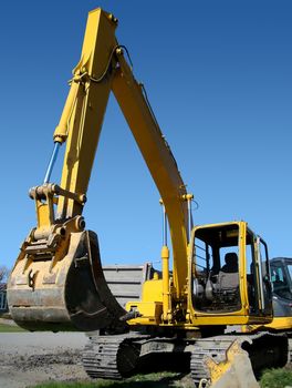 Vertical of mechanical digger in real street urban job site setting contrasted by bright blue sky.