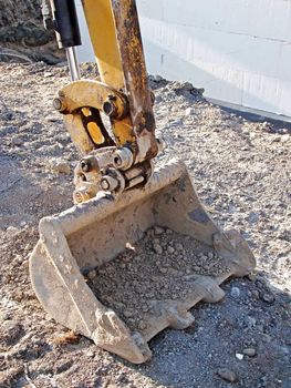 Vertical close up of mechanical digger bucket resting close to new house eco friendly foundations made of styrofoam.