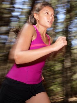 Woman running in forest motion blurred. Asian Caucasian athlete.