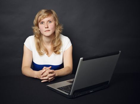 The young woman sits at a table with the computer