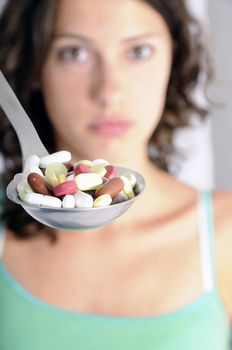 Pretty young woman holding spoon with pile of pills looking skeptical. Concept shot for drug abuse or pharmaceutical industries.