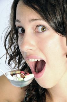 Pretty young woman holding spoon with pile of pills looking skeptical. Concept shot for drug abuse or pharmaceutical industries.