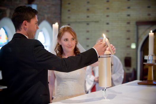 wedding couple lighting the yellow main candle together with their own smaller candles in church during the church ceremony