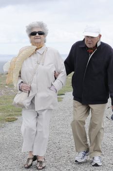Old senior couple walking along the coast holding their hands and smiling.