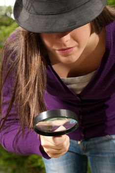 young woman with magnifier glass and hat looking for something on outdoors background