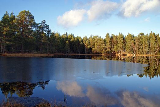 An early winter landscape of a small, partly frozen blue lake and reflections of the sky on its still surface. Photographed in Salo, Finland 7 November 2010.