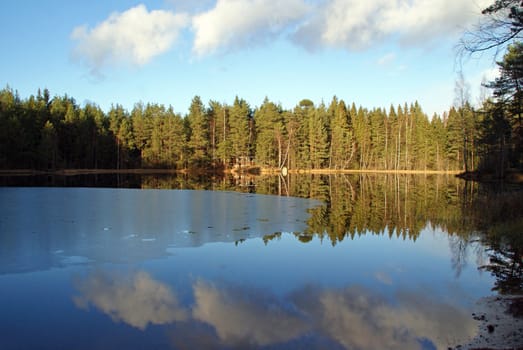 A small, partly frozen lake with the sky and surrounding scenery mirrored on its surface. Photographed in Salo, Finland 7 November 2010.