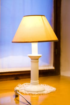 Old lamp on wooden window shelf with dusk in the background.