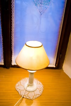 Old lamp on wooden window shelf with dusk in the background.