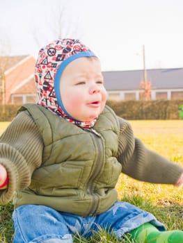 Sweet baby boy outside sitting on green grass laughing