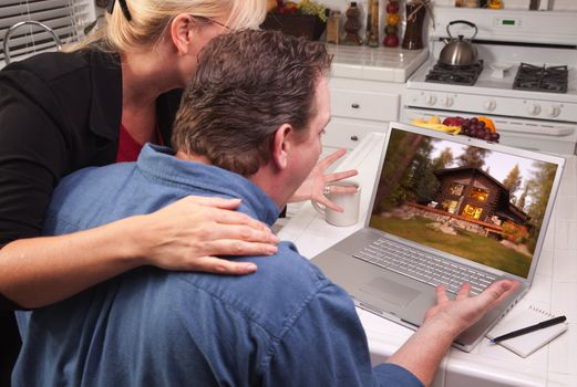 Couple In Kitchen Using Laptop with Lake Cabin on the Screen.