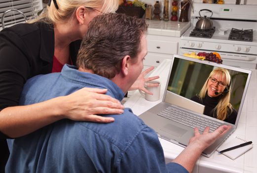 Couple In Kitchen Using Laptop with Customer Support Woman on the Screen.