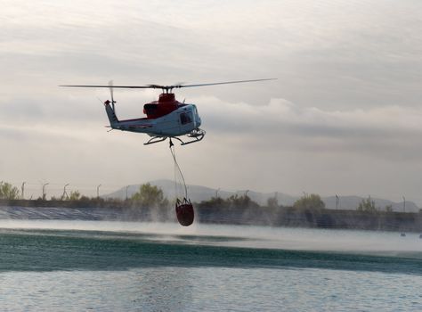 Fire brigade helicopter refilling water while extinguising forest fire
