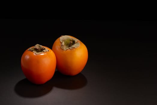 Two fresh persimmon fruits on black with copy space