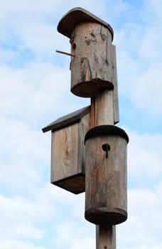 Three wooden starling-houses on background with blue sky and clouds