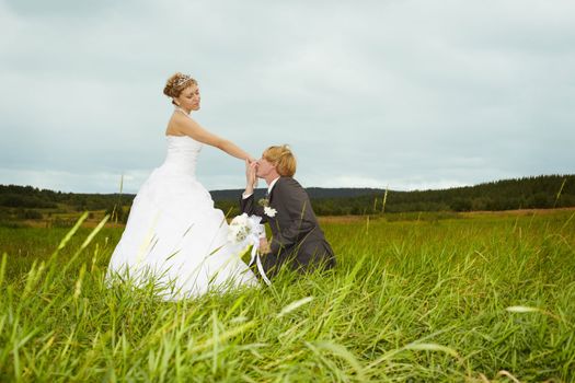 The groom kisses the hand of a young bride in a field