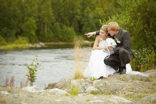 The bride and groom sit on the riverbank