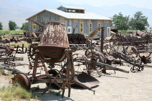 Old-fashioned cement mixer and other antique farming equipment by a storage building in the country